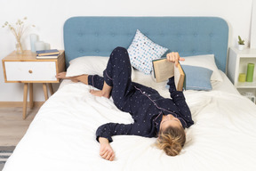 Full-length of a bored young lady trying to read book in bed