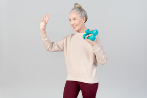 Sorridente donna anziana tenendo i pesi a mano in una mano