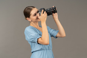 Three-quarter view of a smiling young woman in blue dress taking shot