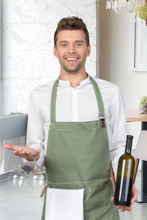 A man holding a bottle of wine and a pair of wine glasses at a restaurant