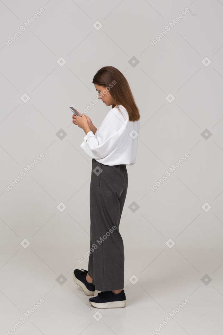 Vista posterior de tres cuartos de una joven en ropa de oficina comprobando la alimentación a través del teléfono