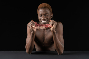 Vista frontal de un hombre afro sonriente mirando la rebanada de carne