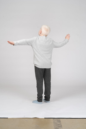 Three-quarter back view of a boy stretching arms to the side