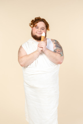 Sonhador jovem homem caucasiano envolto em toalha segurando sorvete