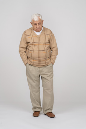 一个穿着休闲服、双手插在口袋里站着的悲伤老人的正面图