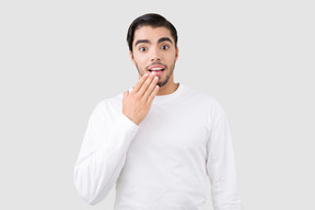 Handsome young man with astonished facial expression holding his hand next to his chin