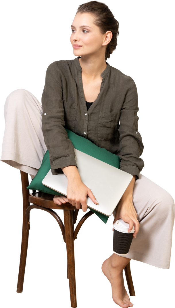 Front view of a young woman sitting on a chair and holding her laptop & touching coffee cup