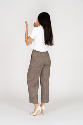 Vista posteriore di tre quarti di una giovane donna in calzoni alzando le mani