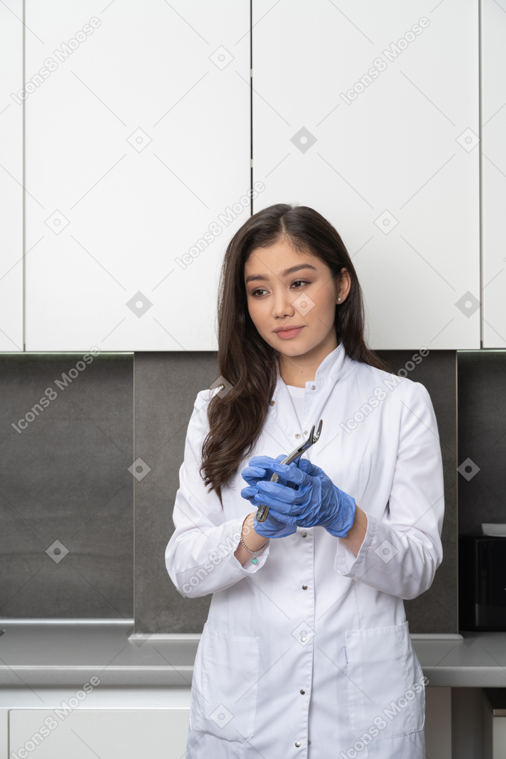 Front view of thoughtful female doctor holding dental instrument and looking aside