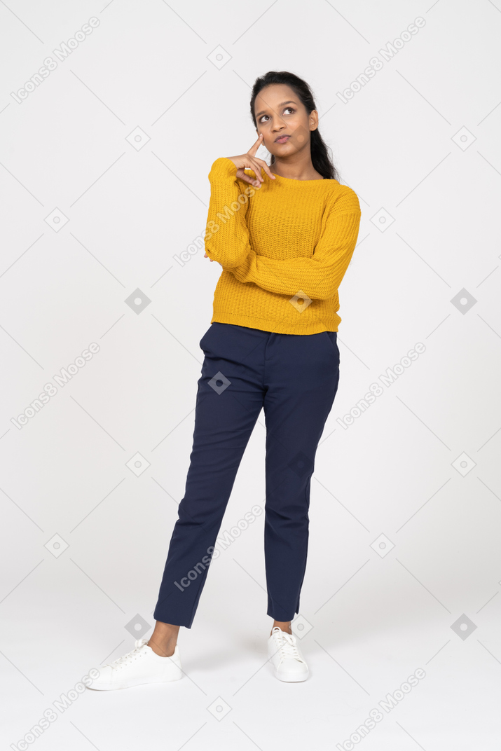 Вид спереди задумчивой девушки в повседневной одежде, смотрящей вверх и касающейся пальцем подбородка