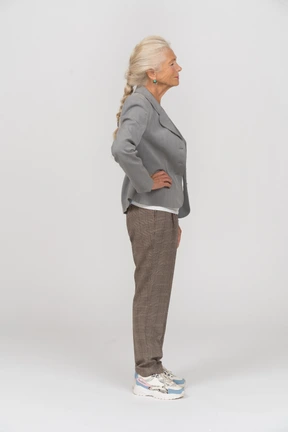 Side view of an old woman in suit posing with hands on hips