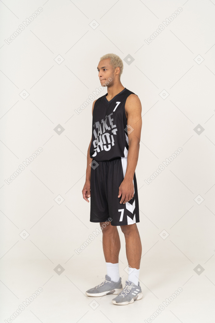 Vista de tres cuartos de un joven jugador de baloncesto masculino de pie y presionando el labio