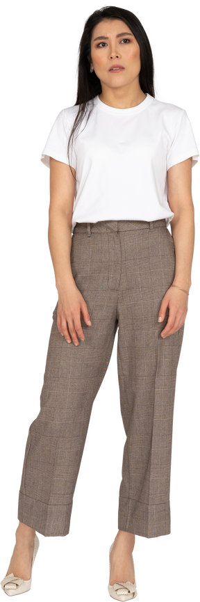 Vista frontale di una giovane donna perplessa in calzoni e t-shirt in piedi che guarda da parte