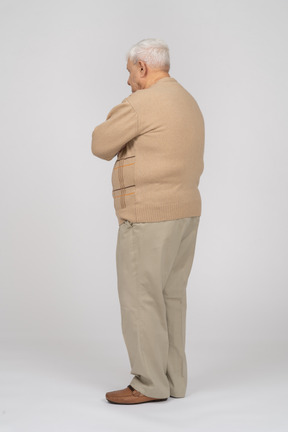 Side view of an old man in casual clothes standing with crossed arms