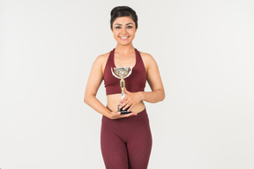 Young indian woman in sportswear holding award cup