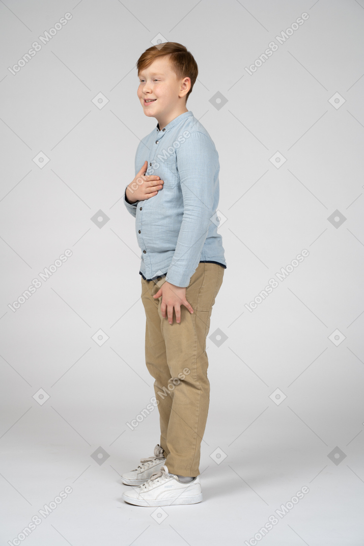 Vista lateral de um menino bonito posando com a mão no peito