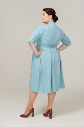 Rear view of a woman in blue dress posing with hands on hips