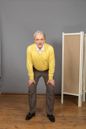 Front view of an old man leaning forward while putting hands on legs