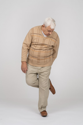 Front view of an old man standing on one leg