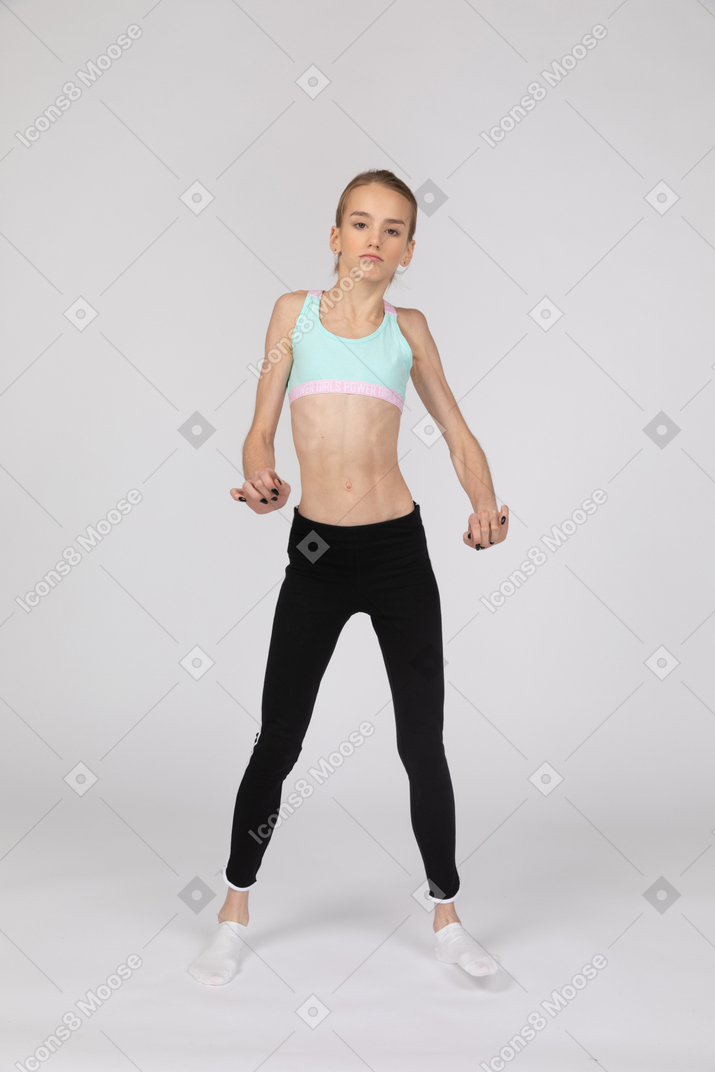 一个十几岁的女孩在运动服在跳舞时举手和她的腿的前视图