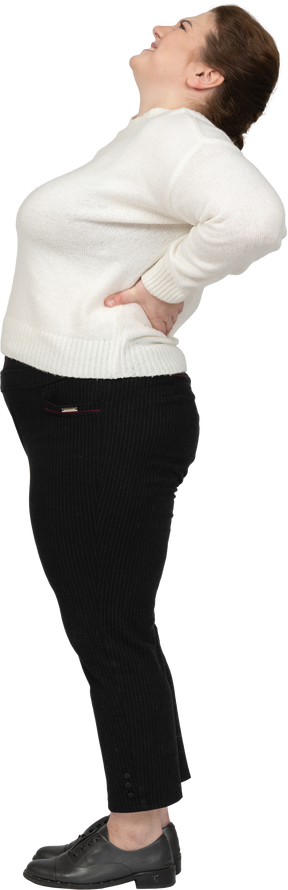 Donna grassoccia in maglione bianco che soffre di dolore nella parte bassa della schiena