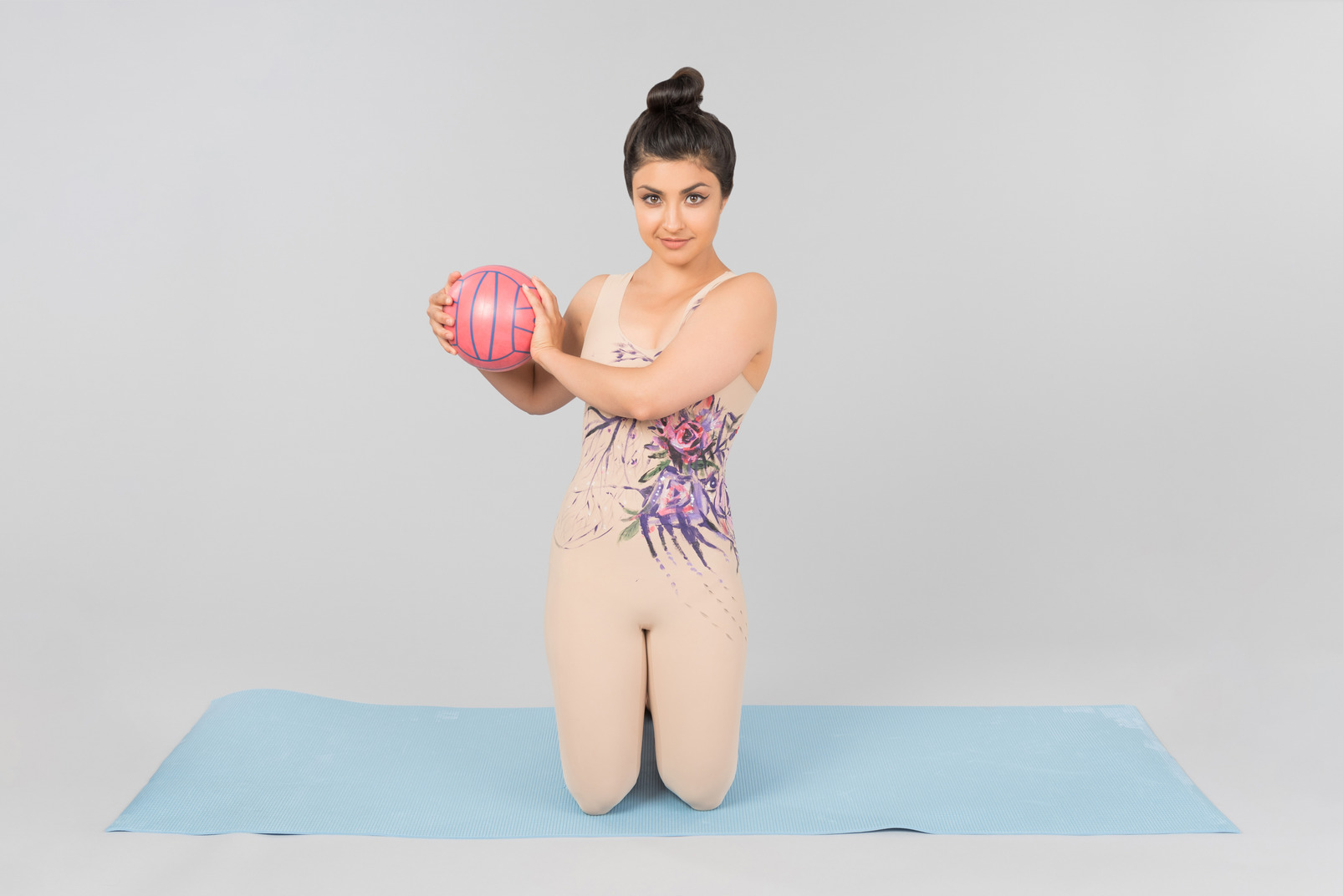 Young indian gymnast sitting on yoga mat and holding ball with both hands