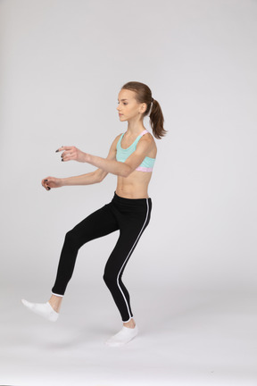 Вид в три четверти девушки-подростка в спортивной одежде, поднимающей руки и ноги