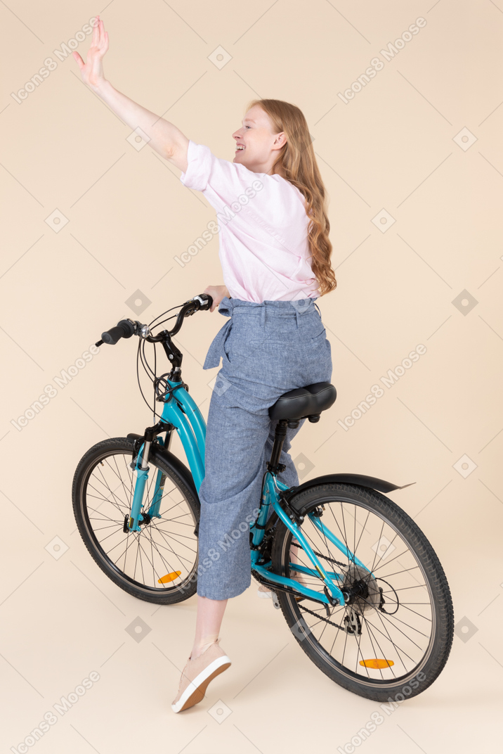 자전거를 타고 손을 흔들며 행복 한 젊은 여자