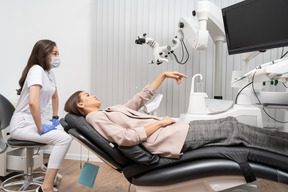 Pleine longueur d'une femme dentiste et sa patiente pointant de côté