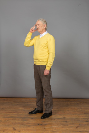 Vista de três quartos de um velho pensativo vestindo um pulôver amarelo e tocando a testa
