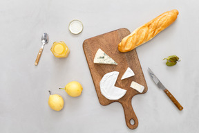 Tabla de cortar con algo de baguette y queso, algunas peras y miel.