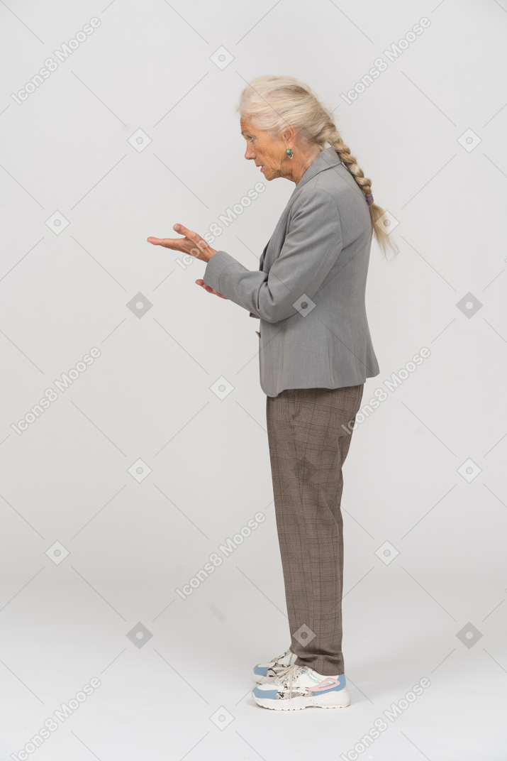 Vista laterale di una vecchia signora in abito che indica con la mano