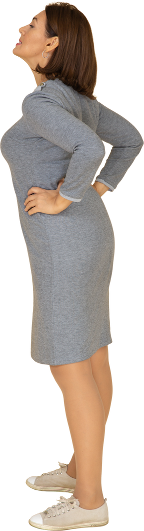 Vista laterale di una donna in abito grigio in piedi con le mani sui fianchi