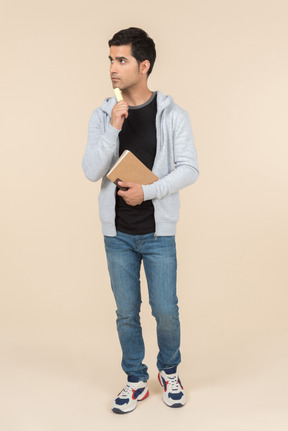 Young caucasian man thinking while holding a notebook and a pen