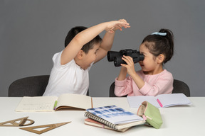 Girl looking through binoculars at the boy being scary