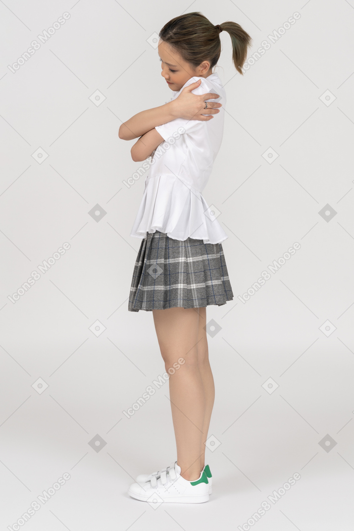 Una ragazza asiatica allegra che si abbraccia lateralmente ad una macchina fotografica
