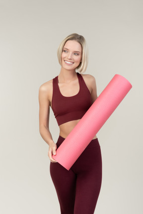 Smiling young woman in sportswear holding yoga mat