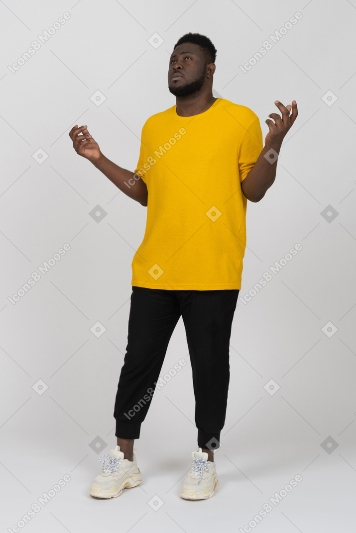 Vista di tre quarti di un giovane uomo dalla pelle scura in maglietta gialla che alza le mani