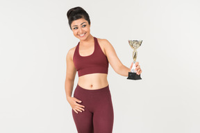 Young indian woman in sportswear holding award cup