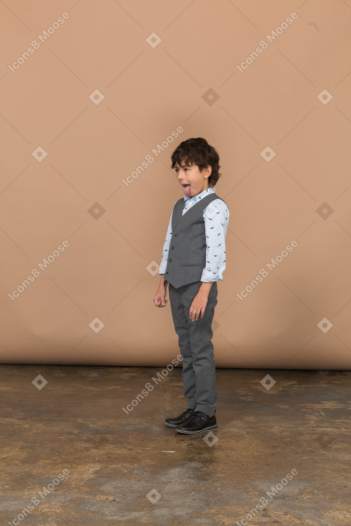 Vista laterale di un ragazzo in abito grigio che mostra la lingua