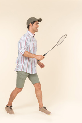 Young caucasian guy standing in profile and holding tennis racket