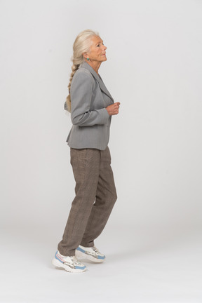 Vista laterale di una vecchia donna in abito grigio che corre