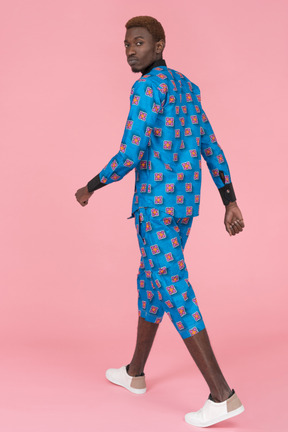 Black man in blue pajamas walking on pink background