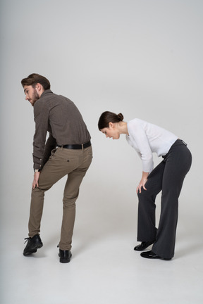 Three-quarter back view of a young couple in office clothing touching knee