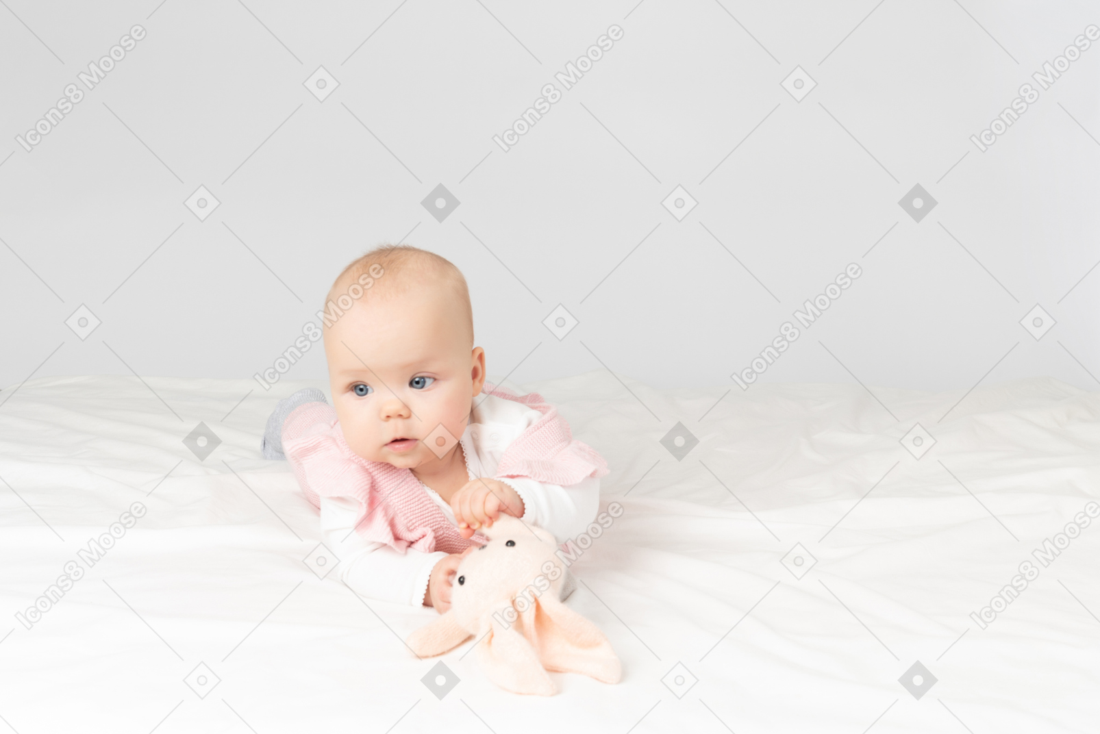 Baby girl lying on stomach and looking on stuffed toy