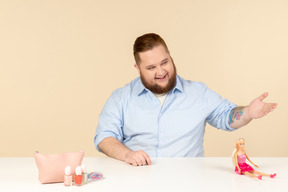 Rindo grande homem sentado à mesa com cosméticos e boneca barbie nele