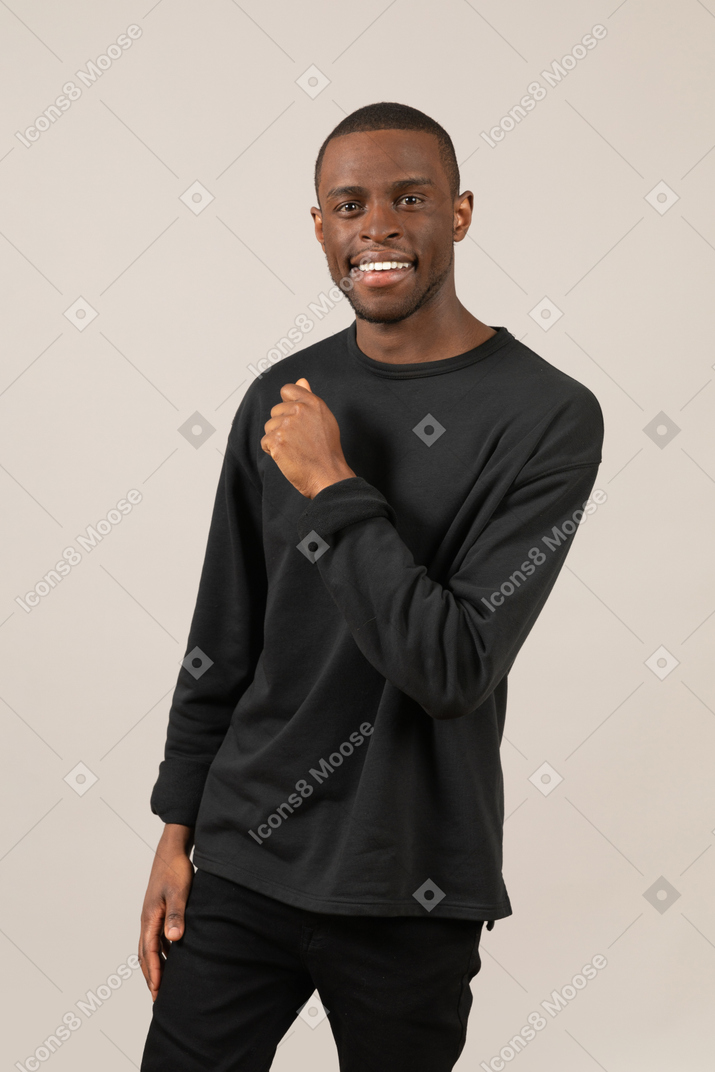 Молодой улыбающийся мужчина стоит с согнутой в локте рукой