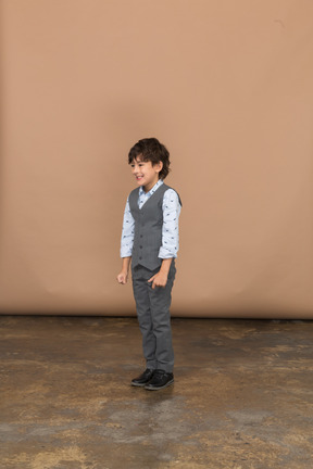 Вид спереди мальчика в костюме, стоящего со сжатыми кулаками