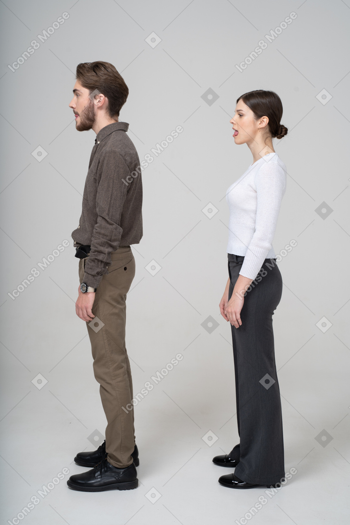 Vista lateral de um jovem casal com roupa de escritório mostrando a língua