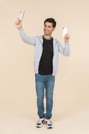 Laughing young caucasian man holding two smartphones